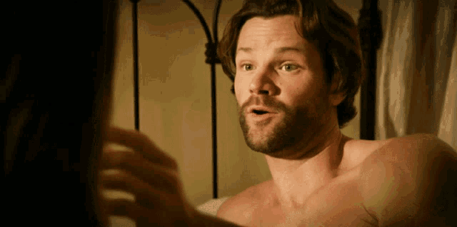 a shirtless man with a beard is looking at a woman 's hand