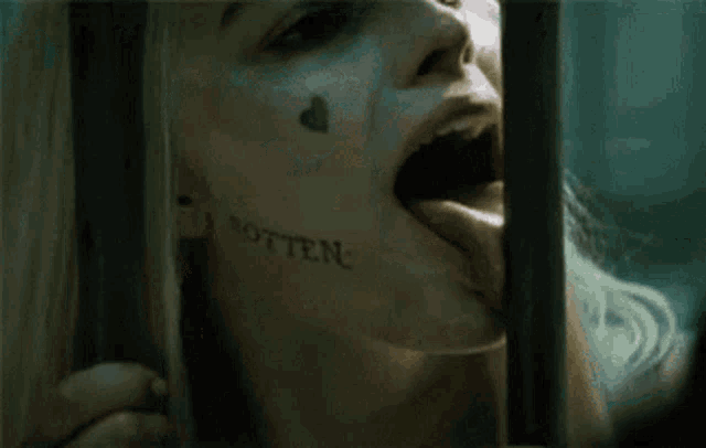 a woman with a tattoo on her face is sticking her tongue out behind a fence .