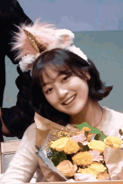 a girl wearing a cat ear headband is holding a bouquet of flowers
