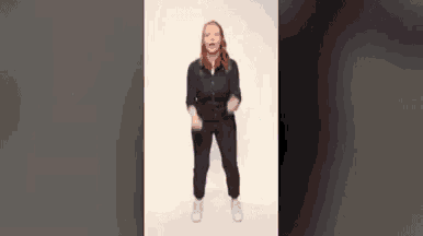 a woman is standing in front of a white wall and dancing .