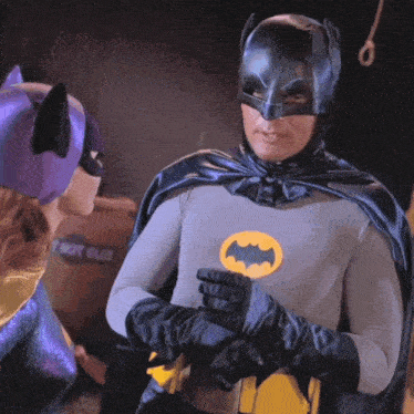 a man in a batman costume stands next to a woman in a purple cat mask