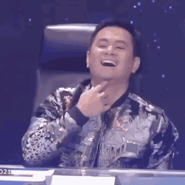 a man is sitting in a chair laughing and pointing at his face .