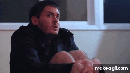 a man in a black jacket is sitting on the floor with his legs crossed and a make a gif.com link in the corner