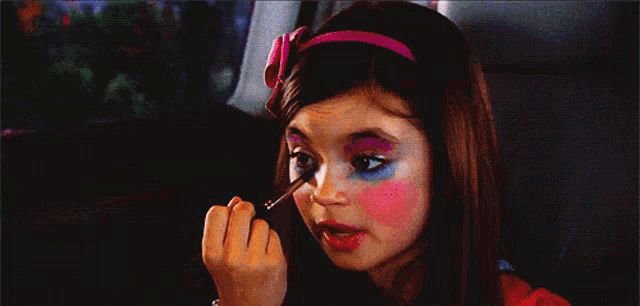 a little girl is applying makeup to her face in a car