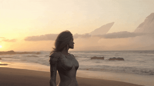 a woman in armor stands on a beach looking at the ocean