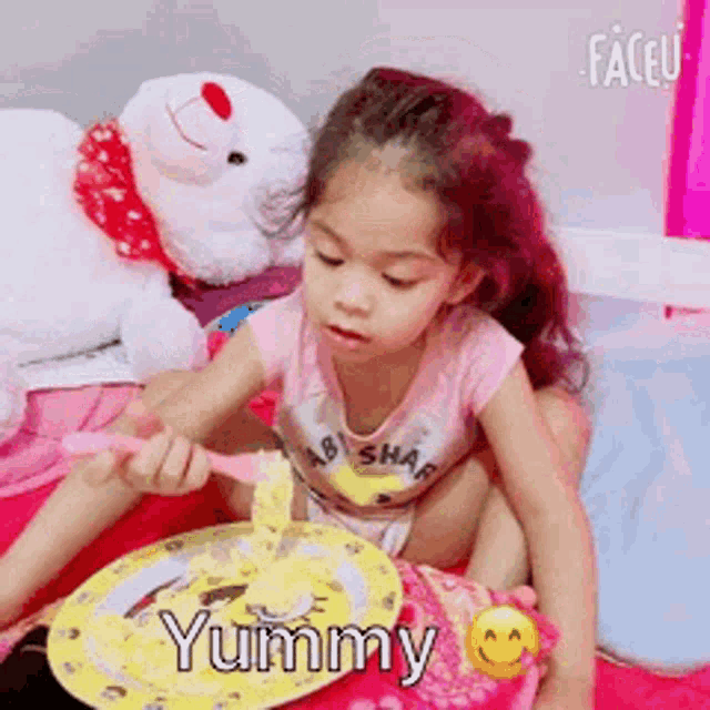 a little girl is sitting on a bed with a plate of food and a teddy bear .