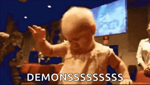 a baby is dancing in front of a screen that says demonssssss