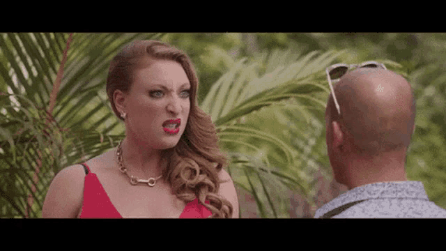 a woman in a red dress is making a funny face while talking to a bald man