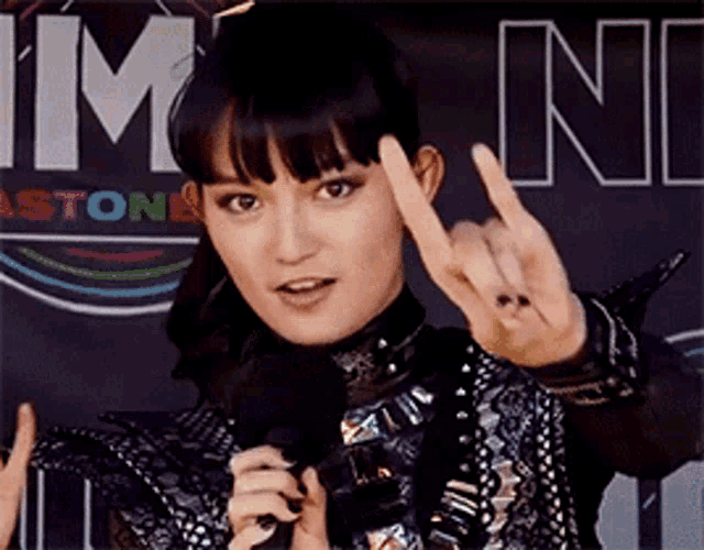a woman giving the horns sign while holding a microphone in front of a sign that says im on it