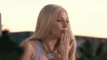 a woman with long blonde hair is blowing a kiss with her hand .