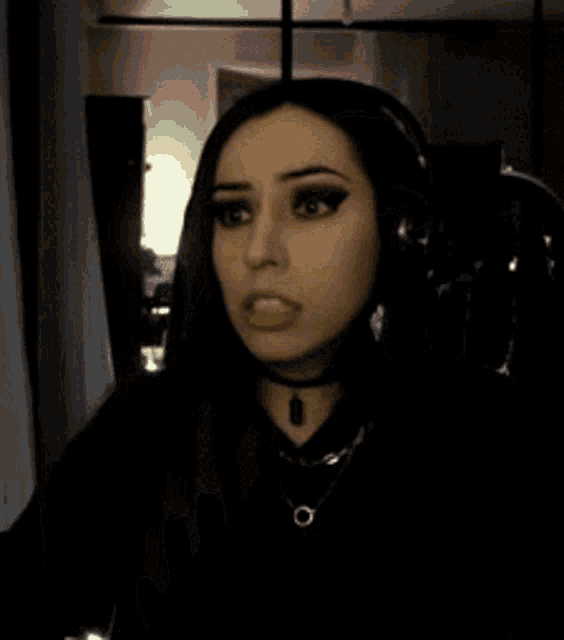 a woman is waving her hand at the camera while wearing headphones and a choker .