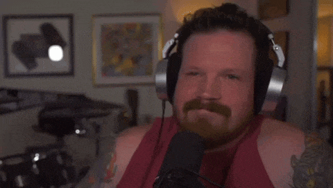a man with a beard is wearing headphones and a red tank top while talking into a microphone .
