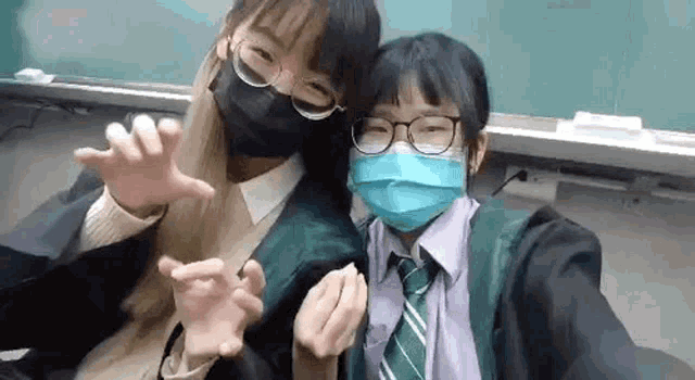 two girls wearing face masks and glasses are posing for a picture in a classroom .