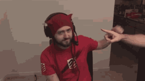 a man wearing headphones and a red hat is pointing at another man .