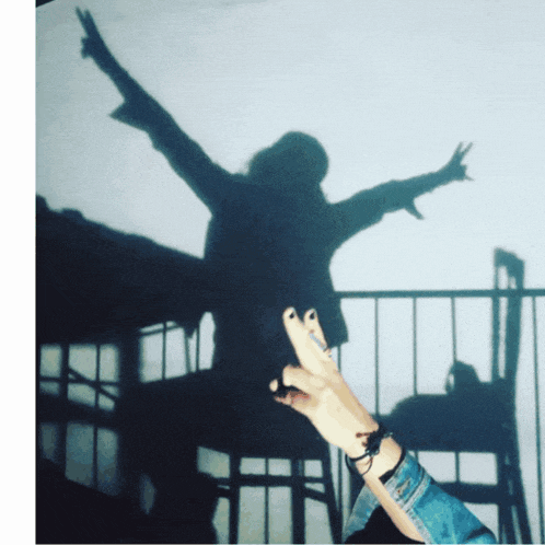 a shadow of a person with their arms outstretched giving a peace sign