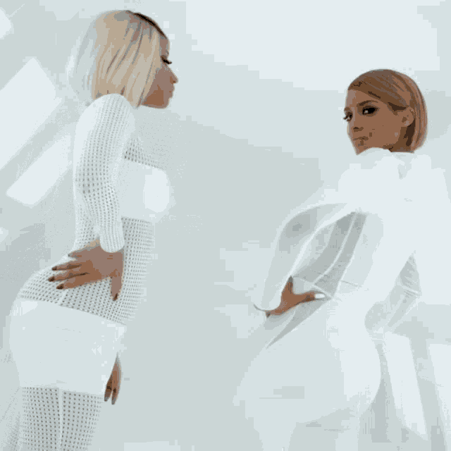 two women are standing next to each other in white jumpsuits