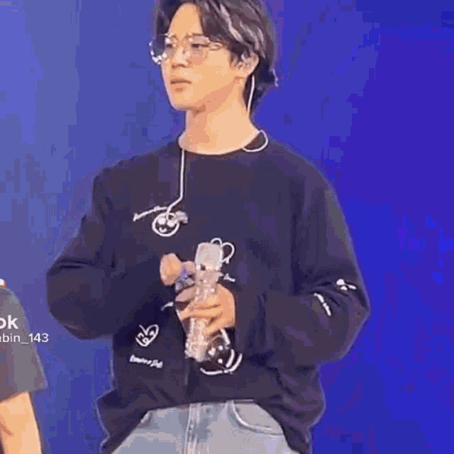 a young man wearing glasses and a black sweatshirt is holding a microphone on a stage .