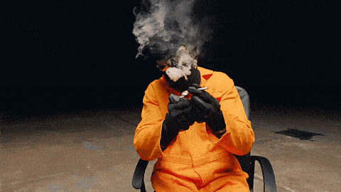 a man in an orange jumpsuit and black gloves is smoking a cigarette