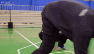 a man is kneeling down on a basketball court with the word dream written on the wall behind him .