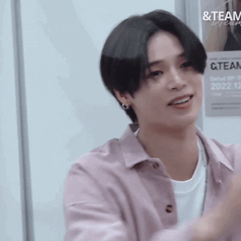 a young man wearing a pink shirt and a white t-shirt is smiling .