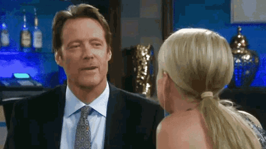 a man in a suit and tie talking to a woman in a ponytail