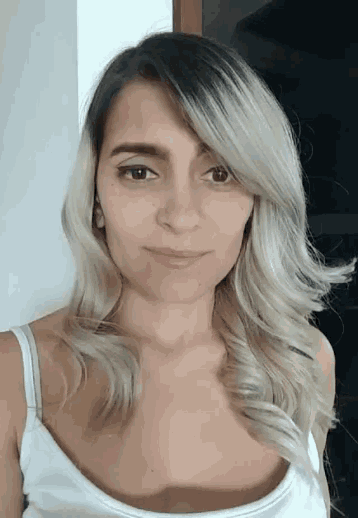 a woman with blonde hair and a white tank top is smiling