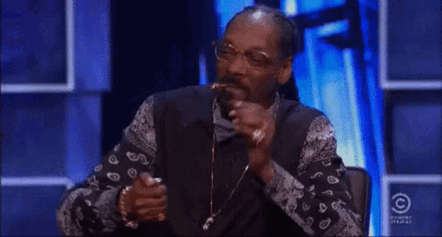 snoop dogg is blowing smoke out of his mouth while sitting on a stage