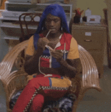 a man wearing a blue head scarf is sitting in a wicker chair knitting