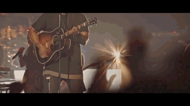 a man playing a guitar and singing into a microphone on stage