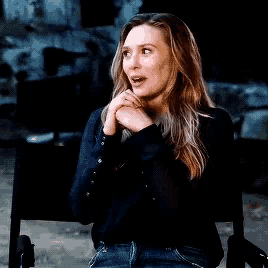 a woman is sitting in a director 's chair with her hands folded and smiling