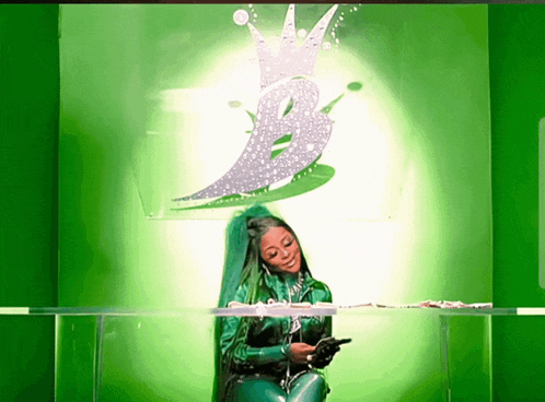 a woman in a green latex suit is sitting in front of a green wall with a crown on it