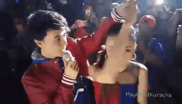 a man in a red jacket is singing into a microphone while a woman in a blue dress is dancing .
