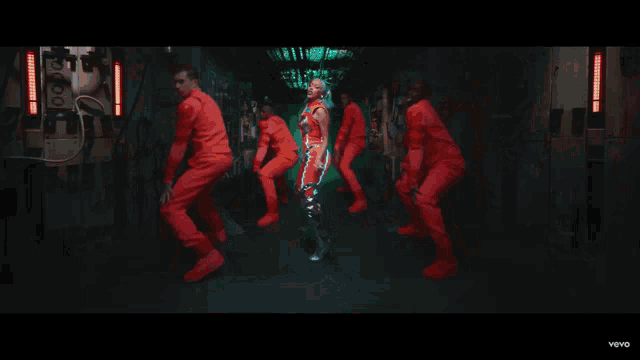 a woman in a futuristic outfit is dancing in front of a group of people