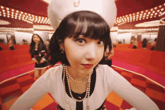 a woman wearing a white hat and pearls is looking at the camera