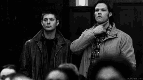 a black and white photo of two men pointing at each other with their fingers .