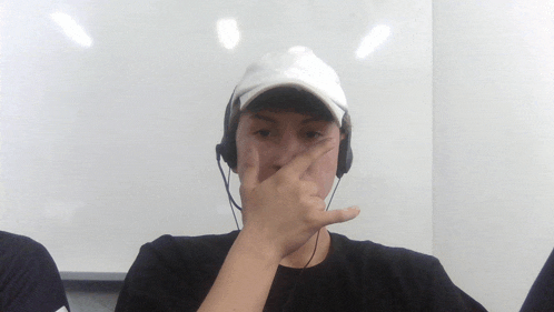 a man wearing headphones and a white hat holds his nose