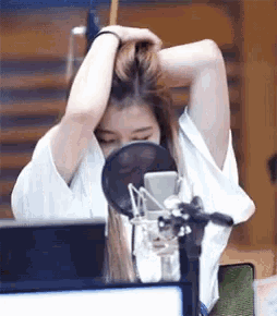a woman is sitting in front of a microphone and holding her hair .