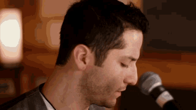 a close up of a man singing into a microphone with his eyes closed