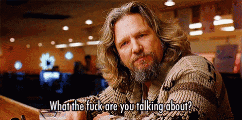 a man with long hair and a beard says " what the fuck are you talking about " while sitting at a table