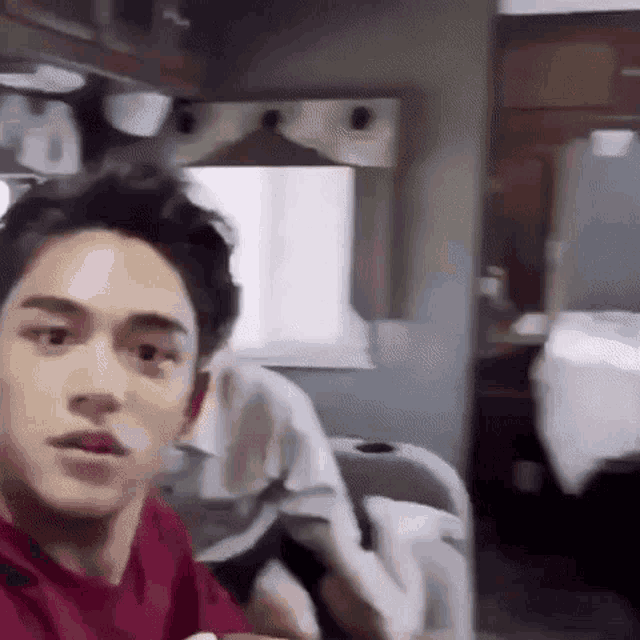 a man in a red shirt is sitting in a room in front of a mirror .