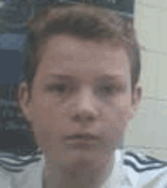 a young boy in a white shirt is looking at the camera .