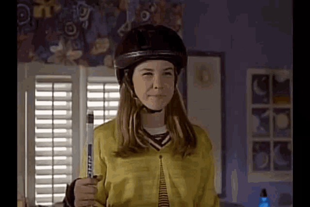 a young girl wearing a helmet and holding a hockey stick is standing in a room .