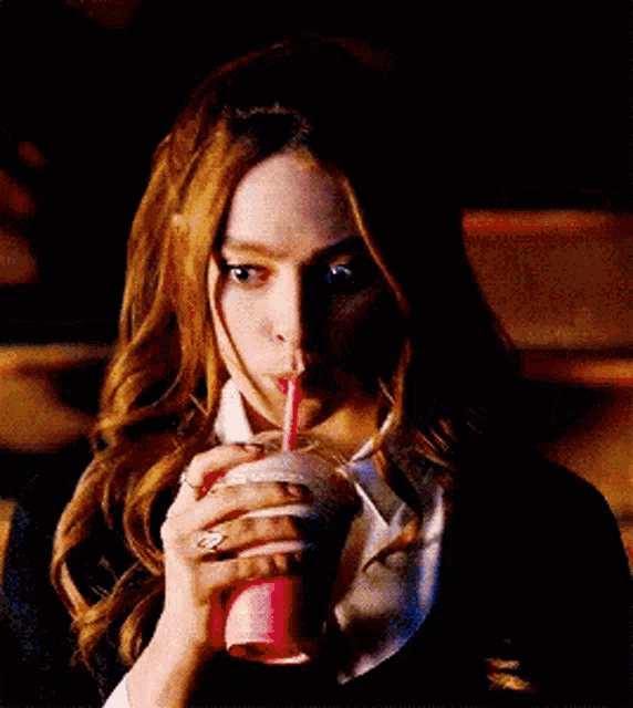a woman with red hair is drinking a pink drink through a straw .