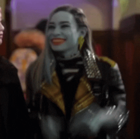 a woman with blue paint on her face is smiling while wearing a leather jacket and gold earrings .