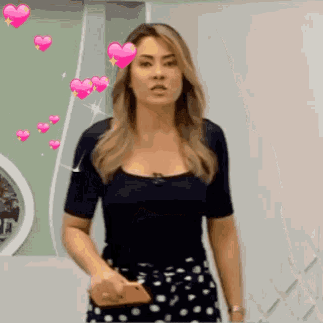 a woman in a black top and polka dot skirt is holding a cell phone with pink hearts around her