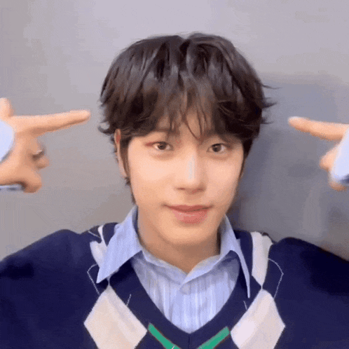 a young man wearing a blue and white sweater is making a peace sign with his fingers .