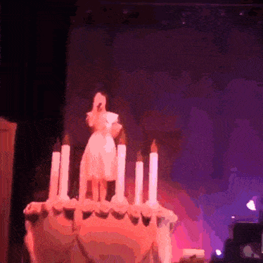 a woman stands on top of a giant cake with candles