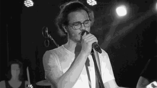 a man with glasses is singing into a microphone on a stage