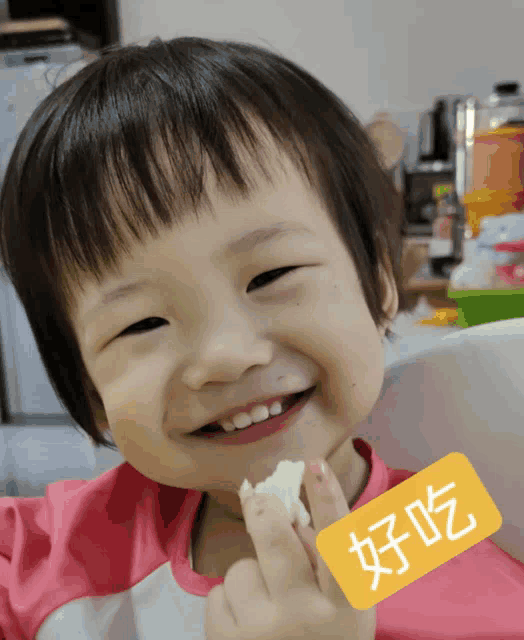 a little girl is smiling while holding a piece of food with a yellow sticker that says ' a ' on it