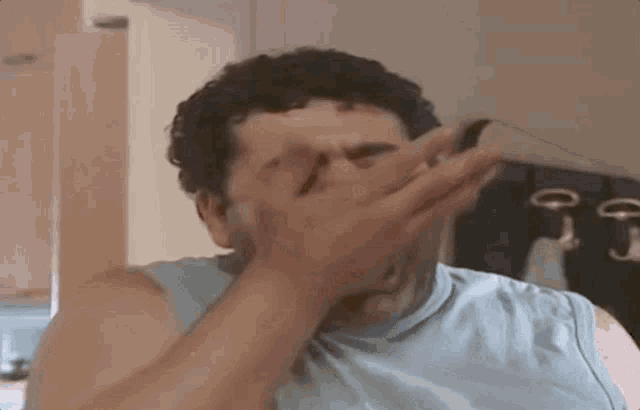 a man covering his face with his hand in a kitchen .